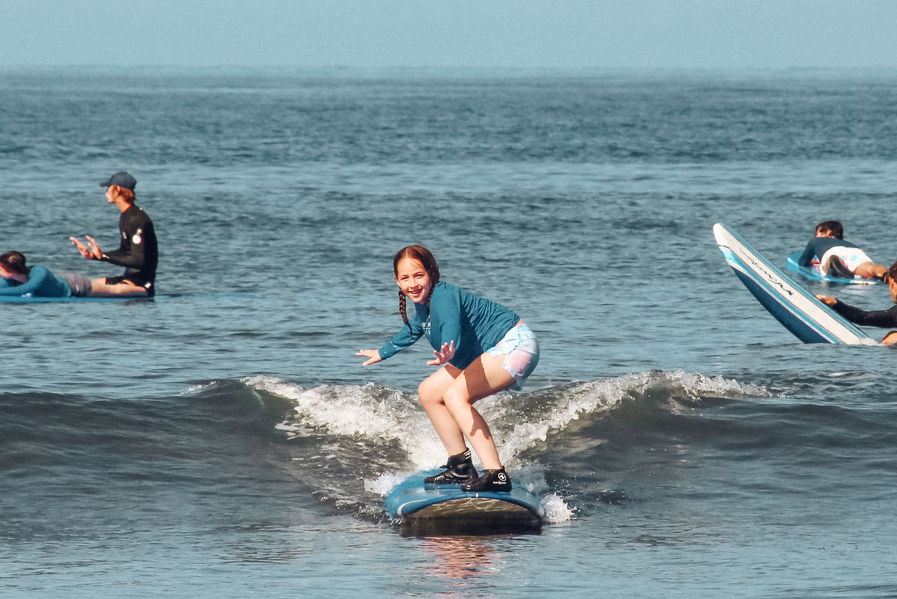 Maui surf instructor in Lahaina balances on a surfboard in the water with a student on his shoulders.