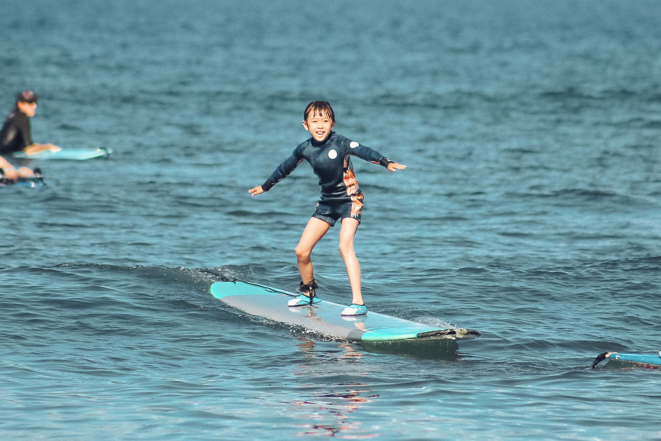 A child catches their first wave during surf lesson at the Guardrails in Maui.