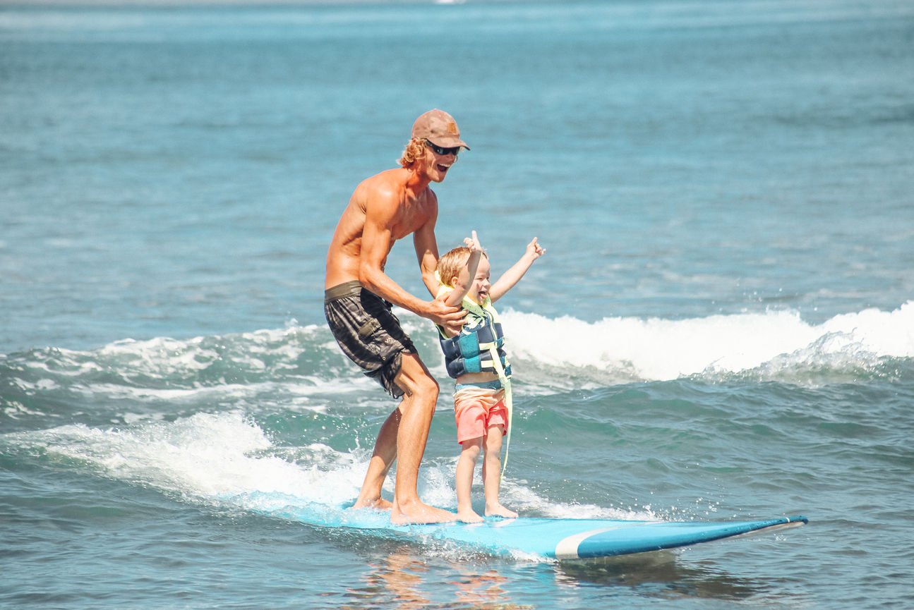 One of Local Pros Maui’s surf instructors smiles while helping a student balance on their surfboard.