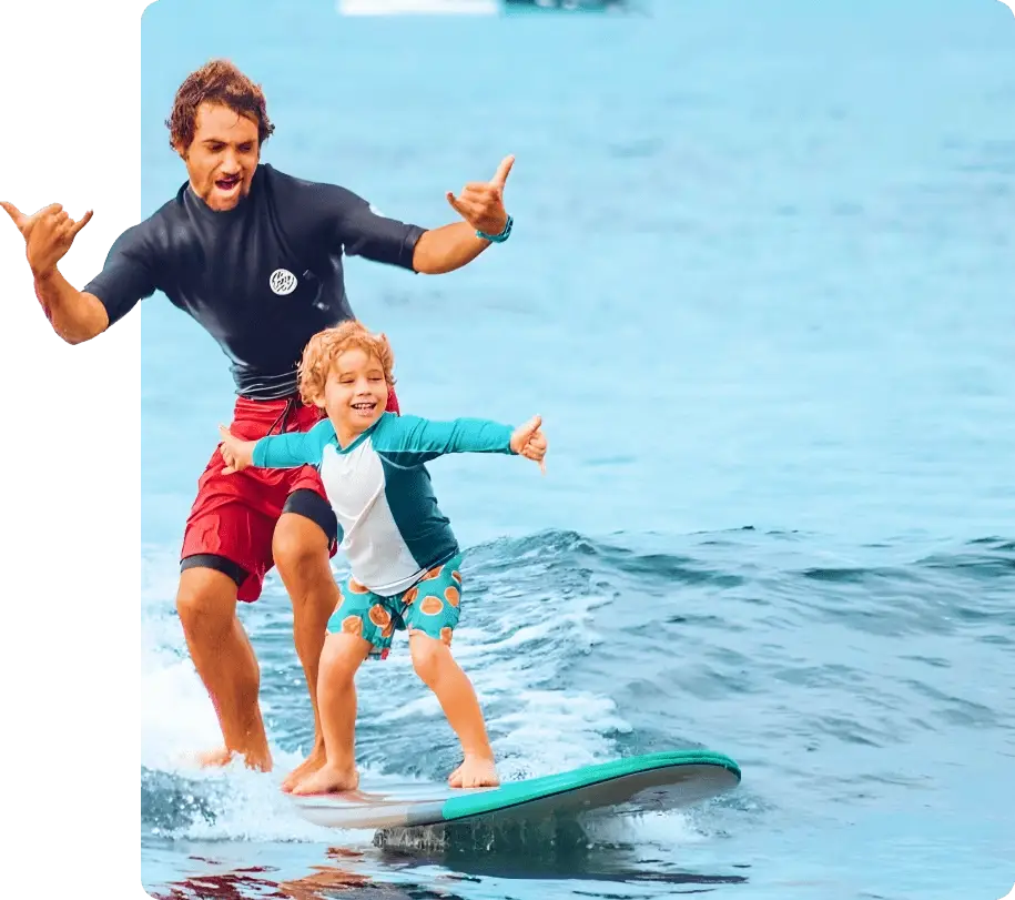 banner-1-1 Instructor cheering with a young child riding a surfboard in Maui