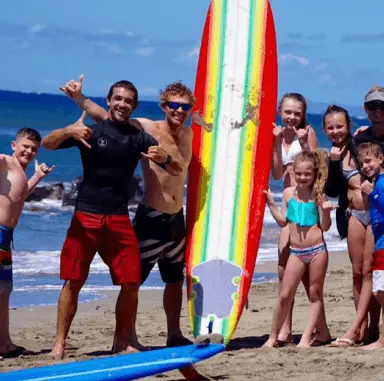 Group of surfers and kids celebrating on the beach with surfboards