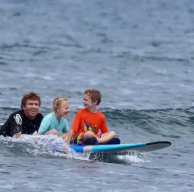 Instructor teaching children on a surfboard in shallow water