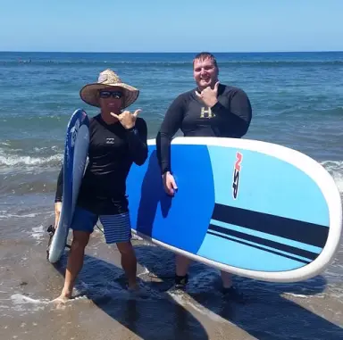 Two surf instructors carrying a paddleboard on the beach
